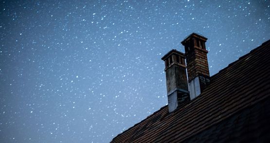 Smalle skorstene på en tagryg mod en stjerneklar nattehimmel